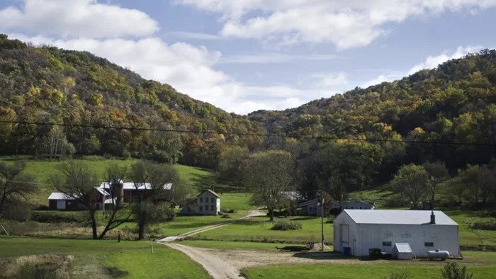 A rural valley farm with a red barn, white farmhouse and outbuildings among forested autumn hills